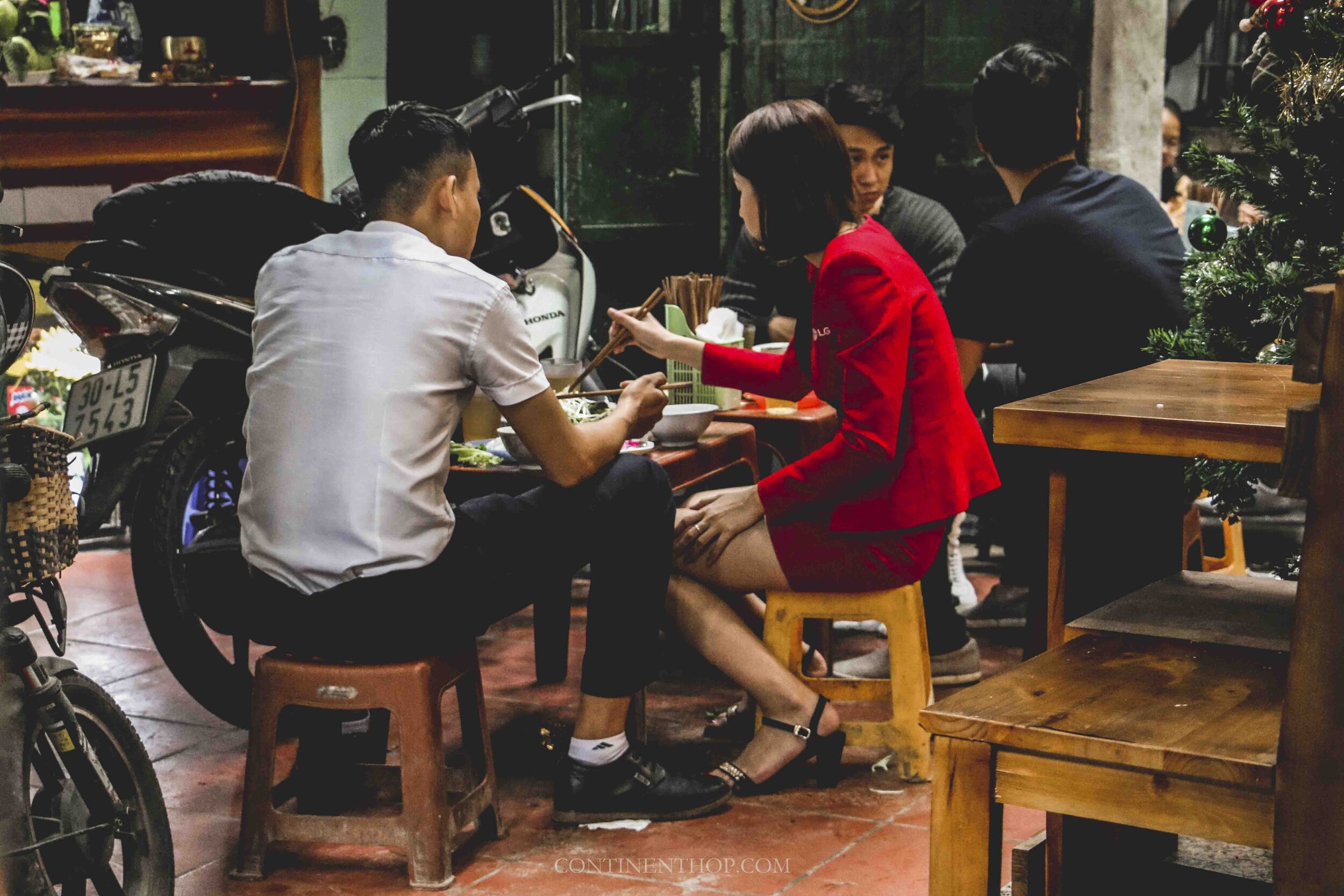 Two people sat on tiny stools sharing a bowl of Pho in Hanoi