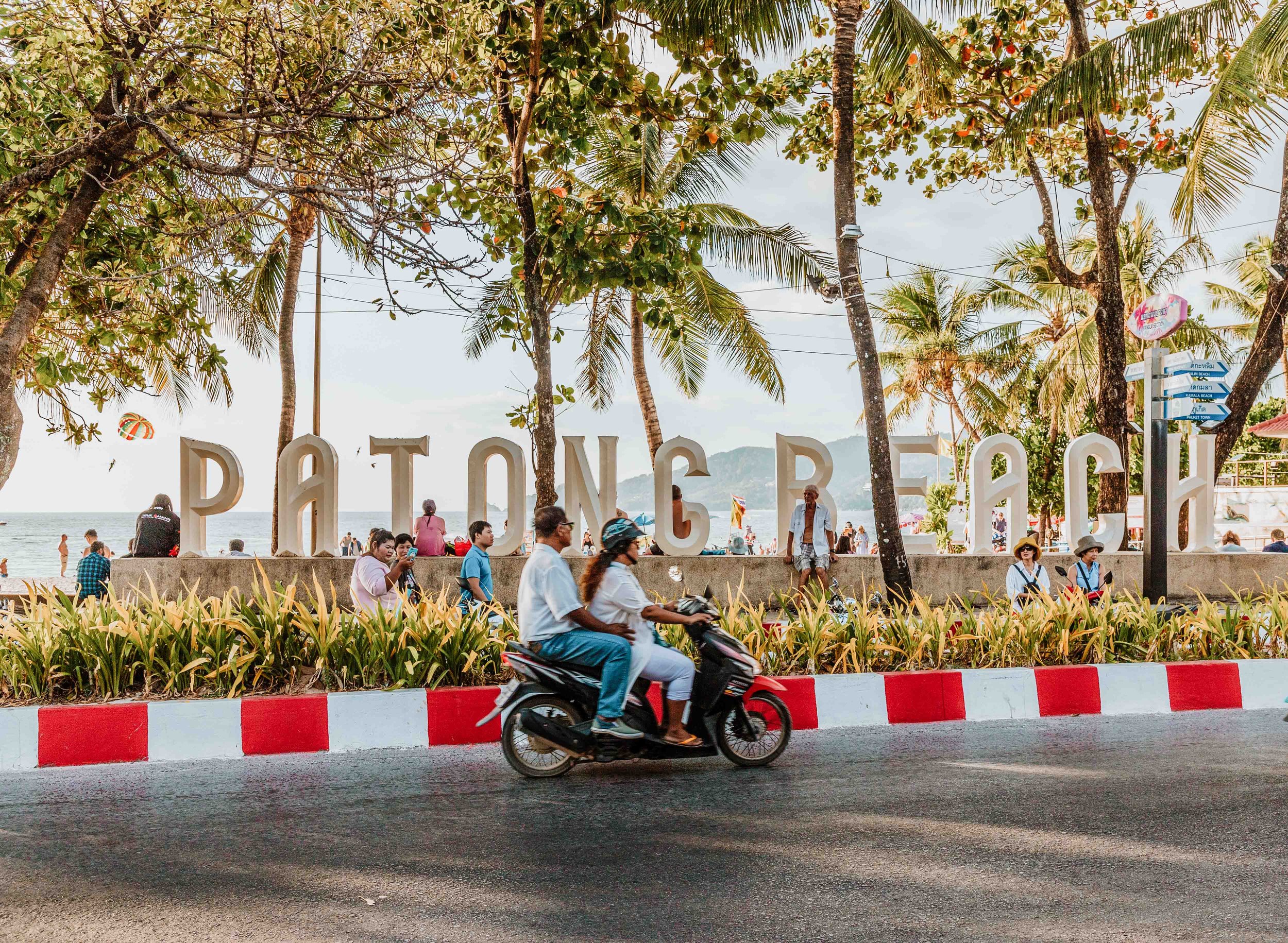 People on a motorbike passing by the Patong Beach sign on a phuket travel itinerary