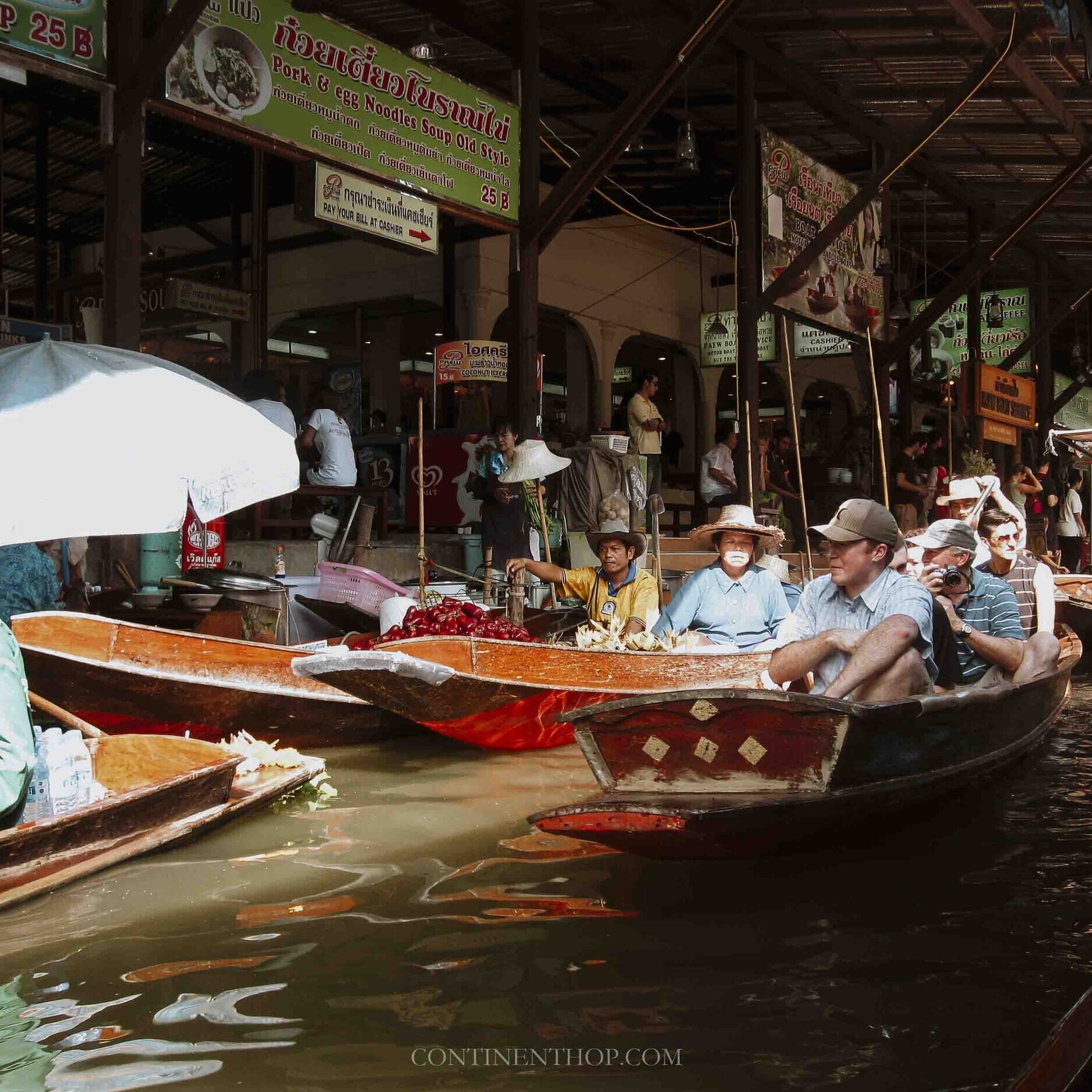 People sat in a boat passing through a floating market - Things to do on your 7 days in thailand itinerary