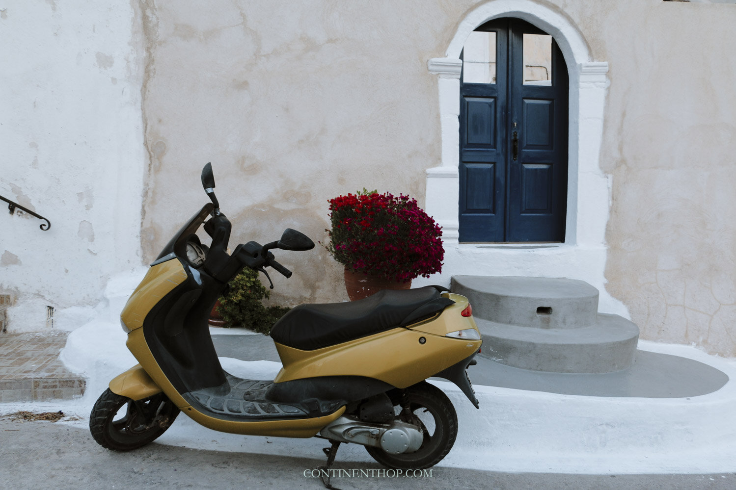 A yellow motor bike in front of a blue door in Emborio Santorii or Emborion