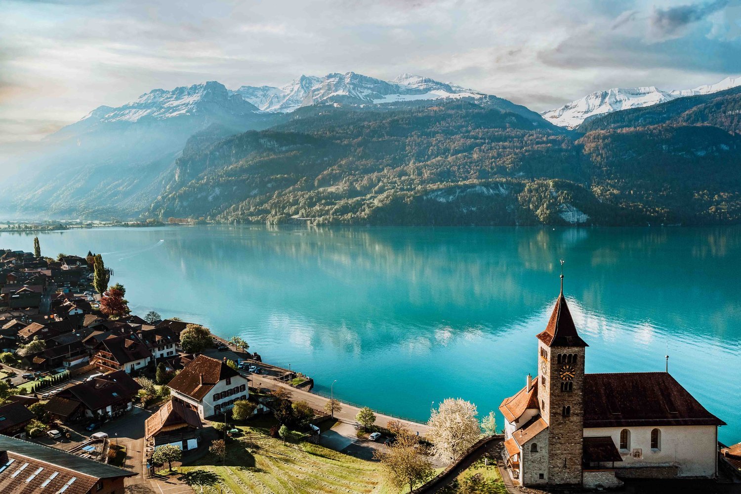 A small church by a bright blue lake with mountains behind unusual european destinations
