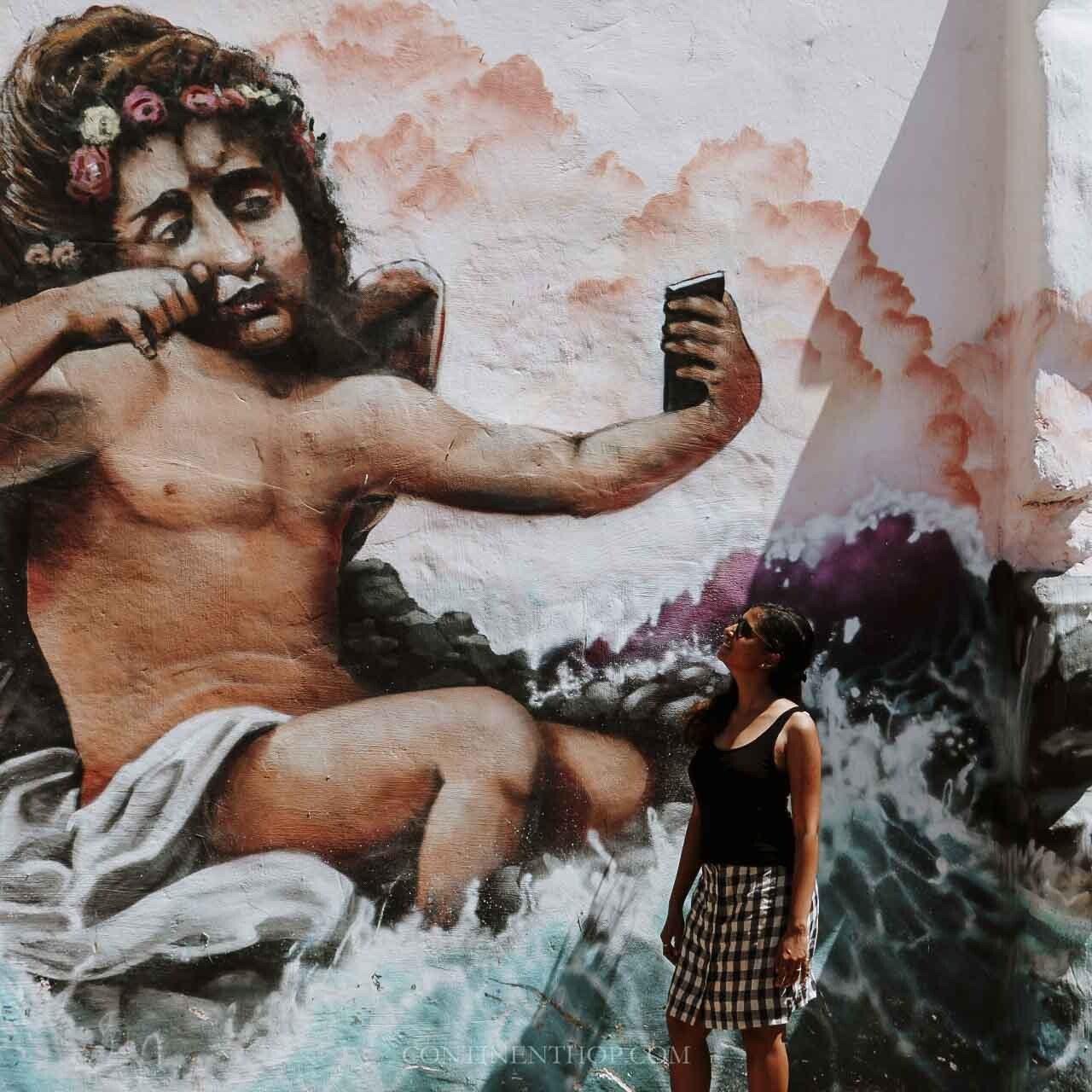 Mural of a cherub holding a phone while woman looks it it from paphos to limassol