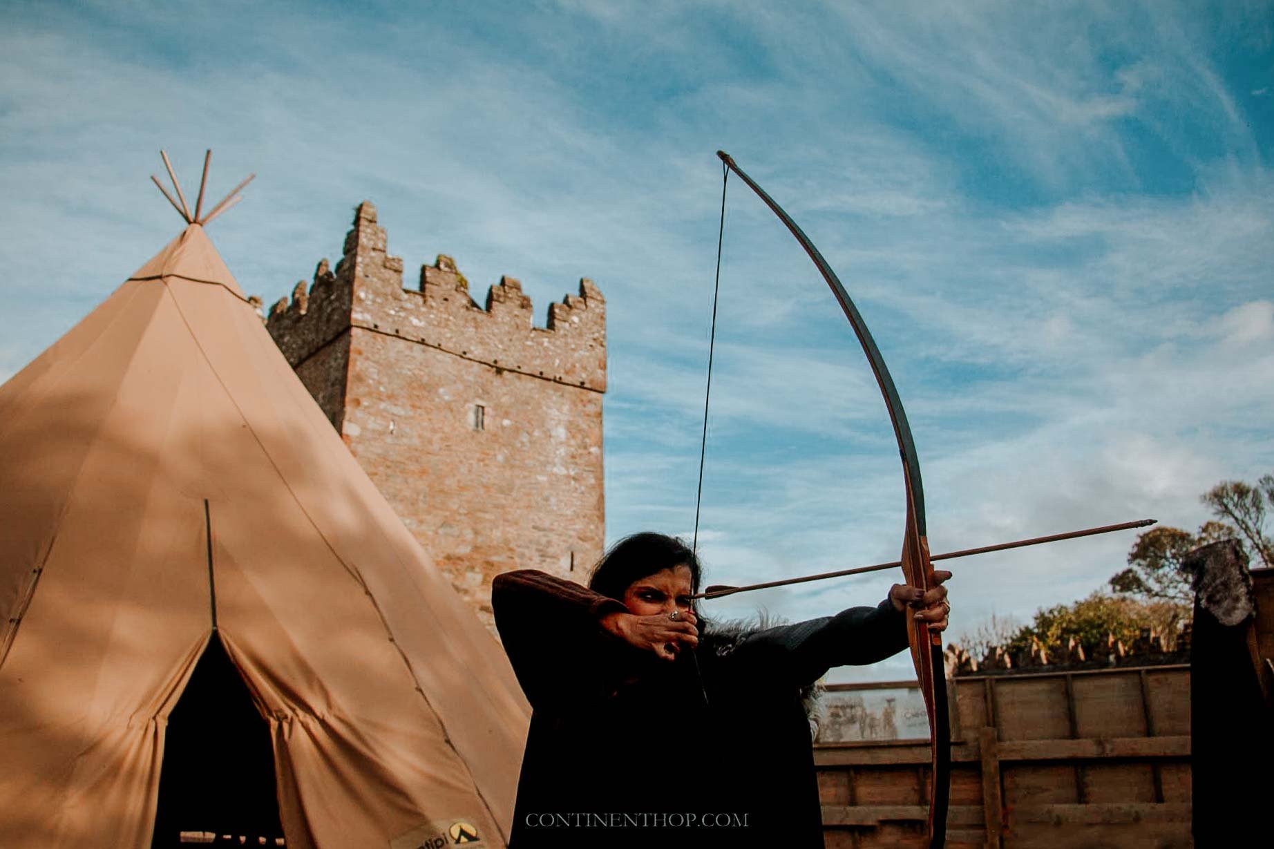 Woman shooting an arrow in front of tepee on a GOT locations in Northern Ireland visit