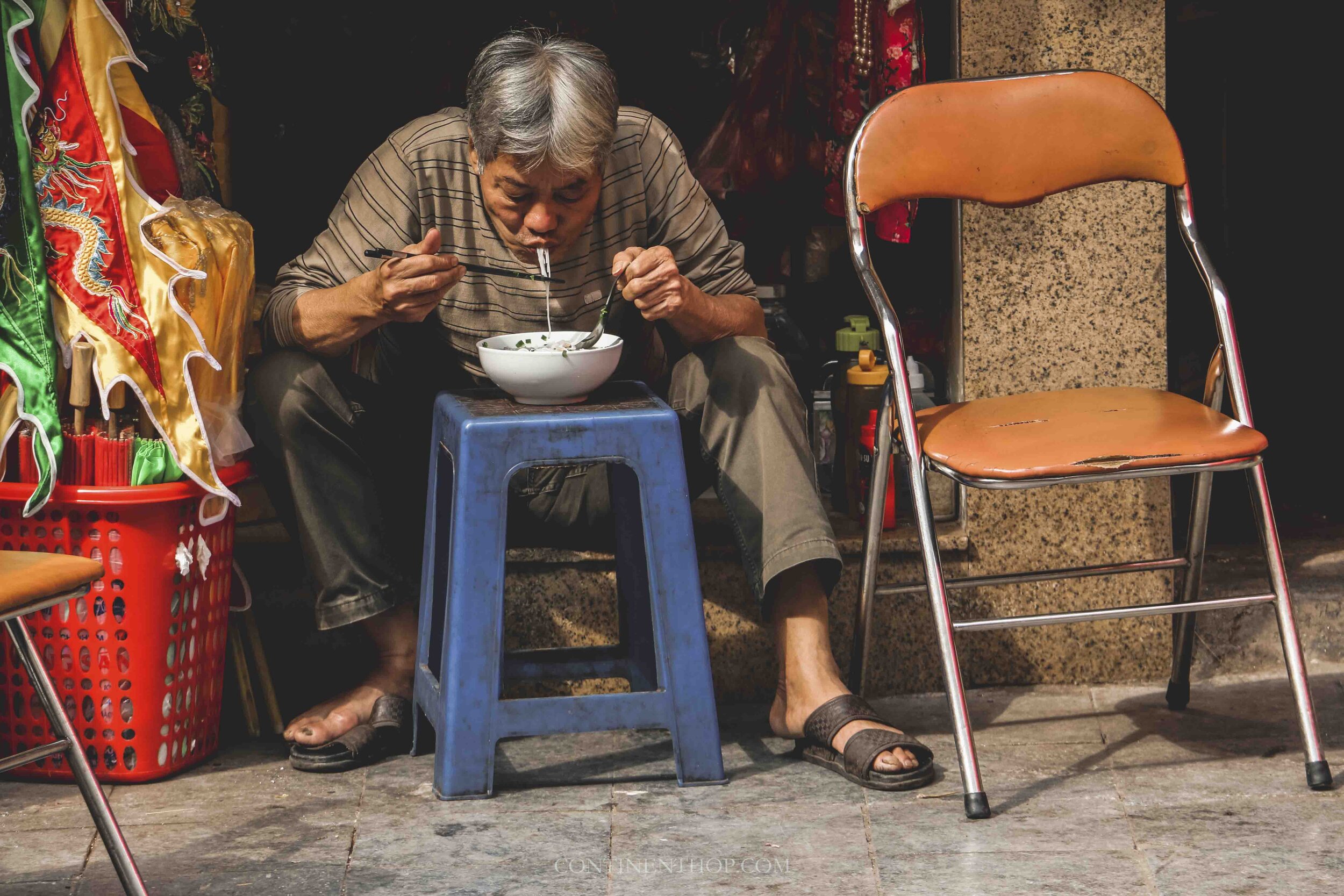 Photo of man in Hanoi Vietnam eating a bowl of Pho outside his shop
