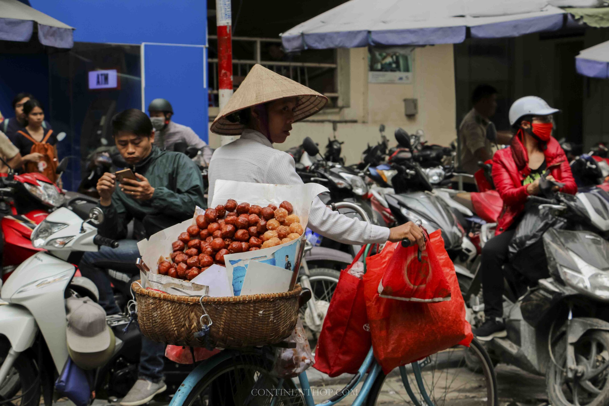 Image of woman in Hanoi Vietnam pushing a bicycle with fruits on it