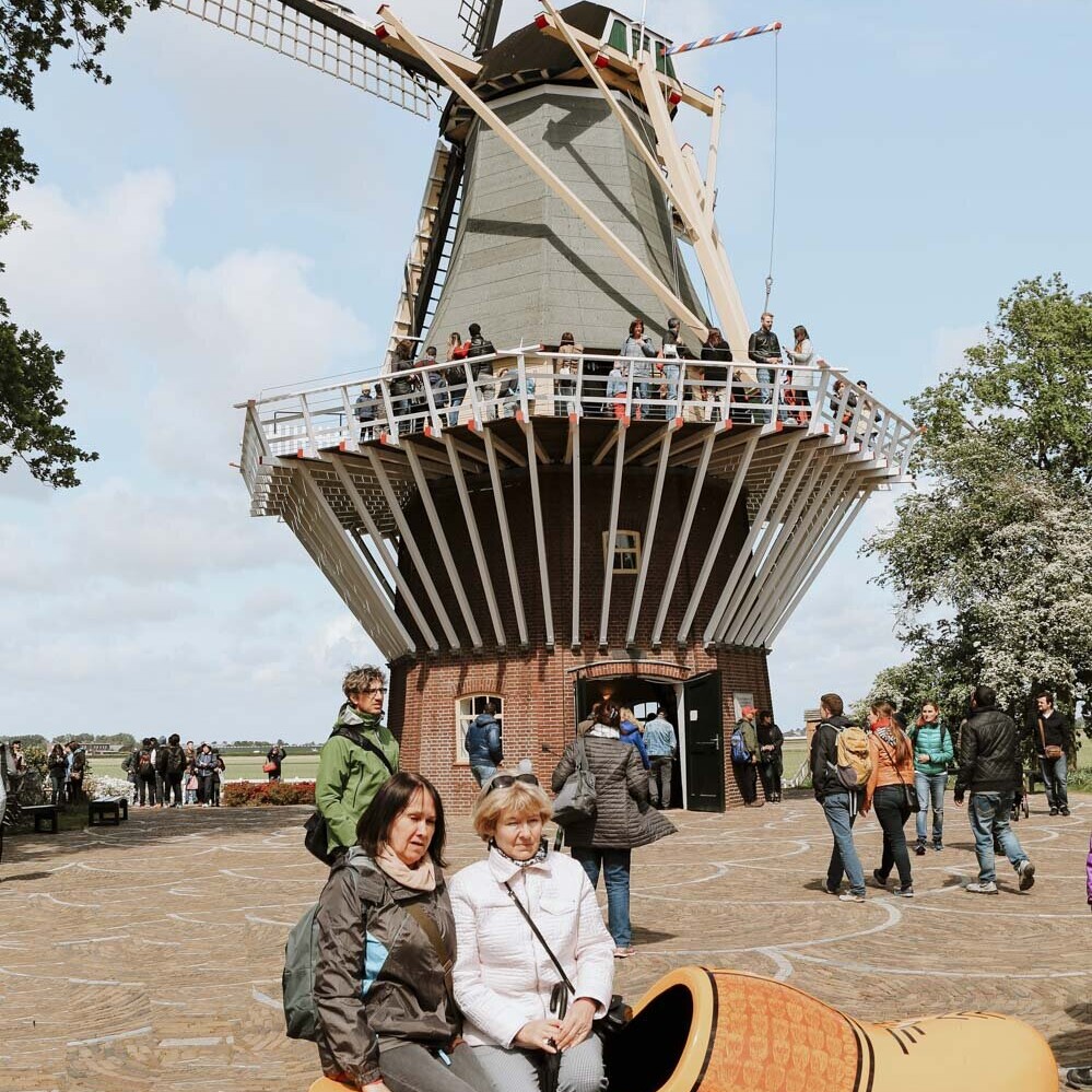 People sitting in a wooden shoe in front of a windmill at Keukenhof gardens at the tulip festival holland