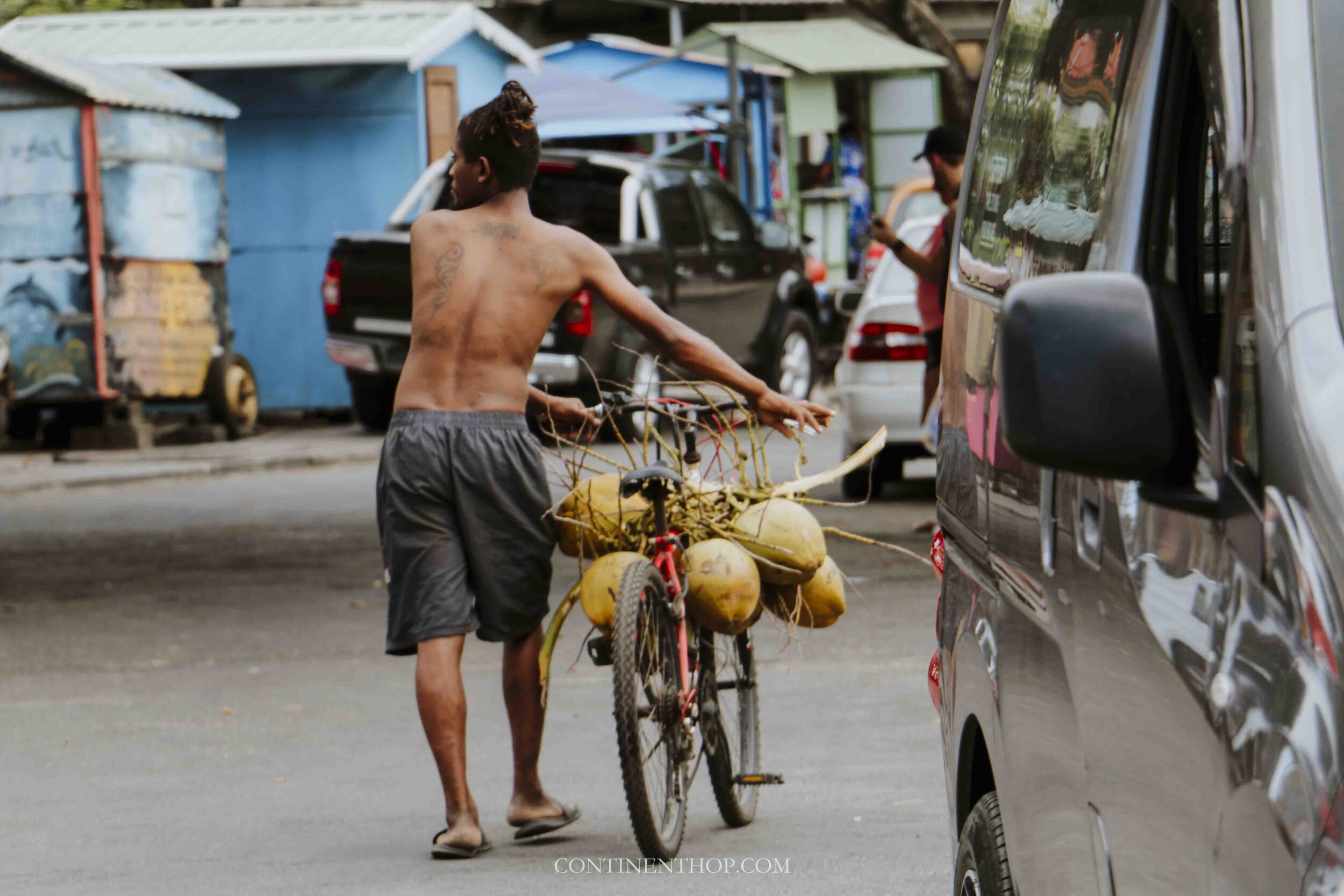 Man walking on the street with coconuts on a bicycle to sell at a Mauritian street food stall