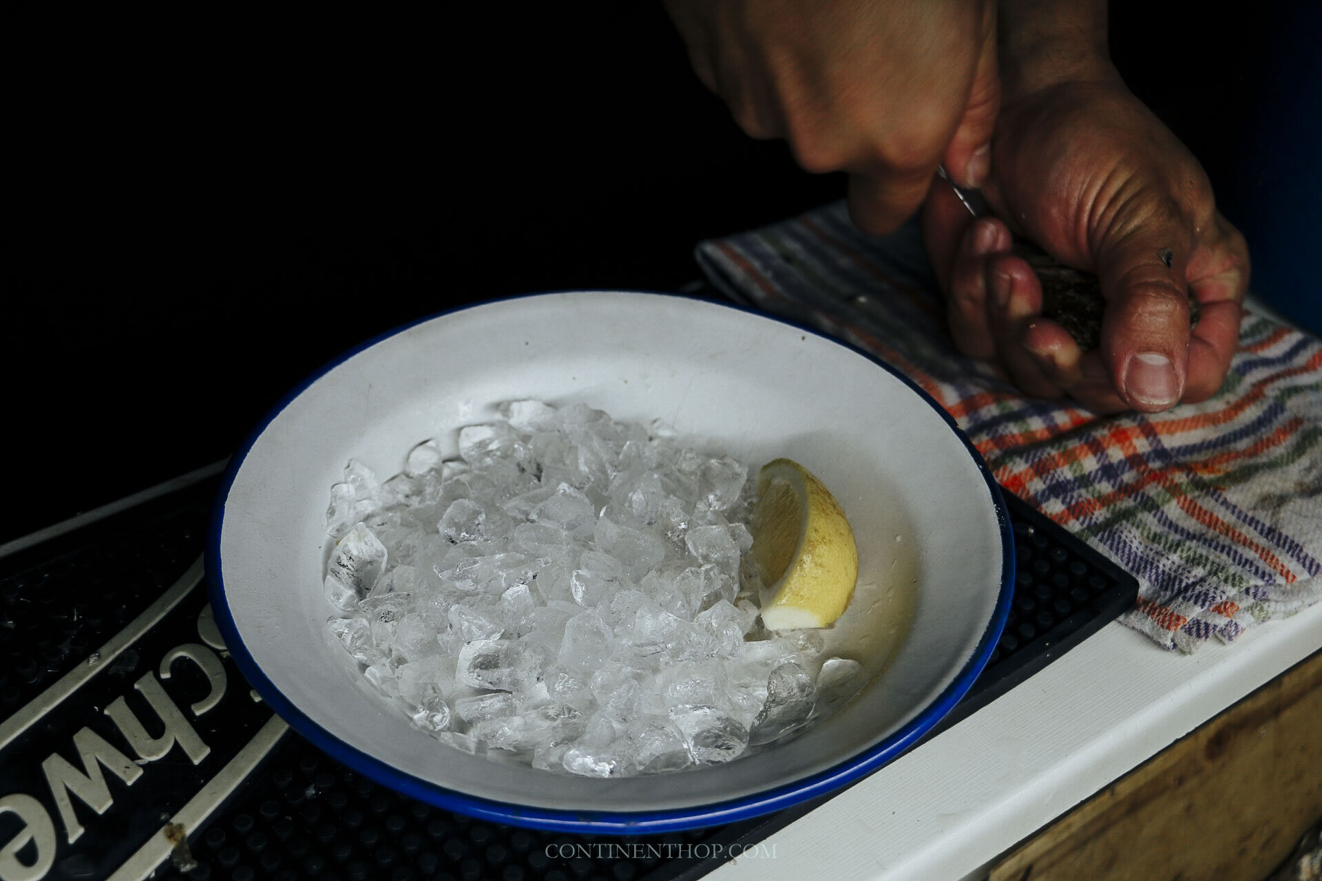 person shucking oysters for tapas in santander spain next to a bowl of ice with lemon slice