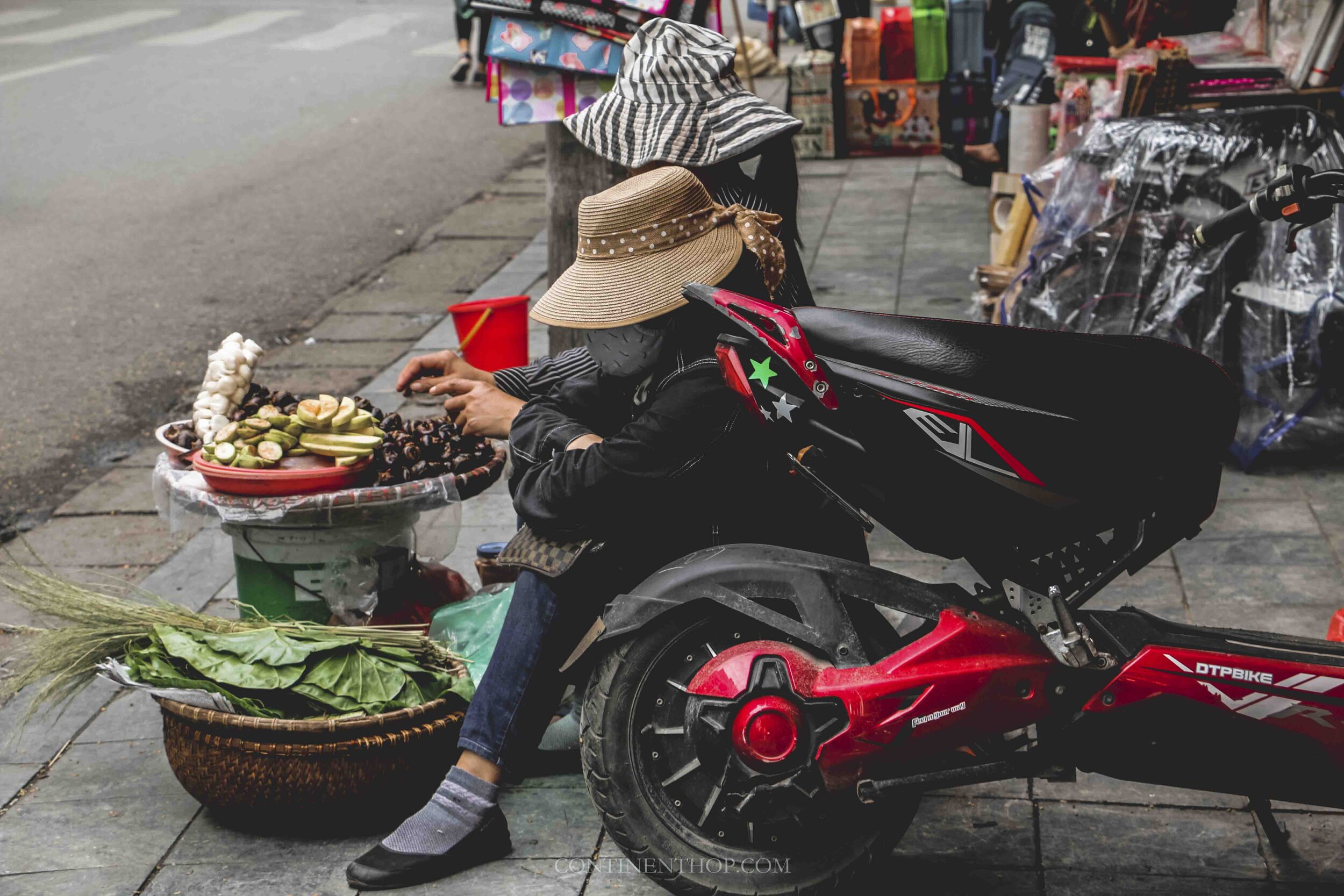 Woman sat next to a motorbike on the road selling local fruits in Hanoi